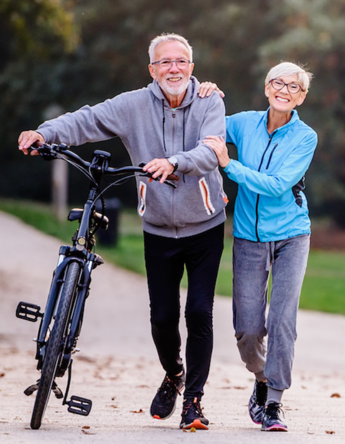 Smiling senior couple enjoying a walk in the park, with one person walking a bicycle, symbolizing restored mobility and health after wound recovery.